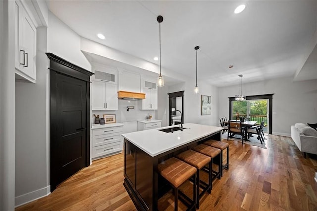 kitchen featuring a sink, light countertops, glass insert cabinets, white cabinetry, and a center island with sink