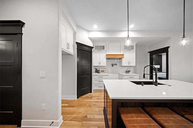 kitchen featuring a sink, white cabinetry, light wood finished floors, light countertops, and pendant lighting