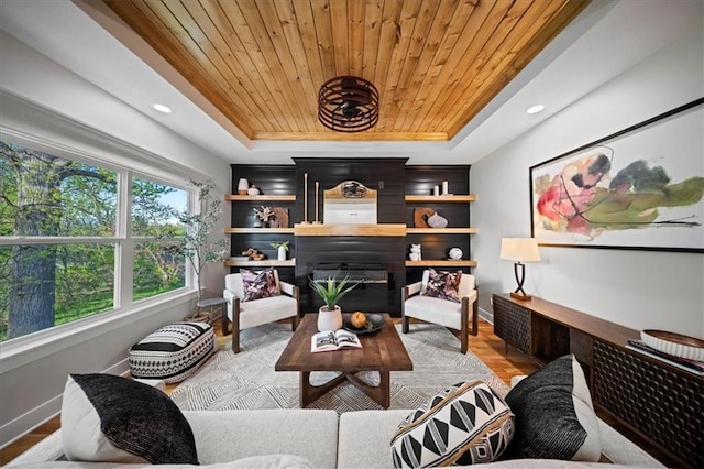 living room with a tray ceiling, wooden ceiling, baseboards, light wood finished floors, and a glass covered fireplace