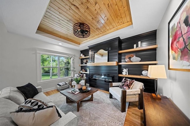 living area with a raised ceiling, wood finished floors, wooden ceiling, baseboards, and a chandelier