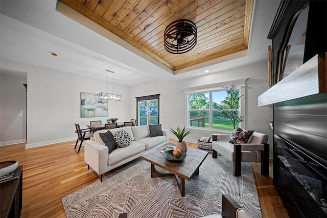 living area with a tray ceiling, wood finished floors, baseboards, wood ceiling, and a chandelier