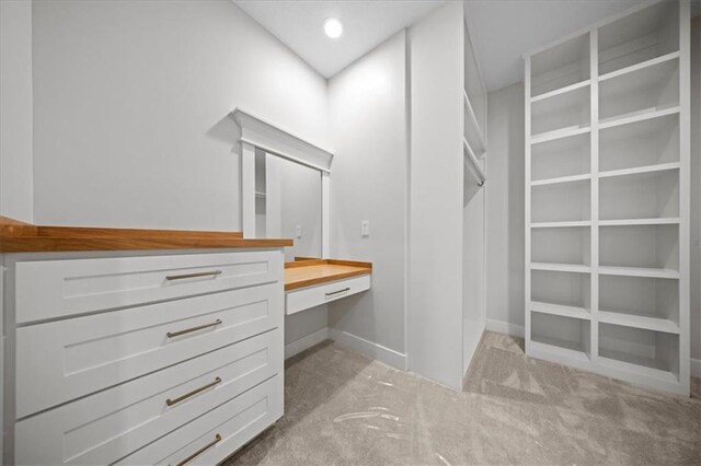walk in closet with built in desk and light colored carpet