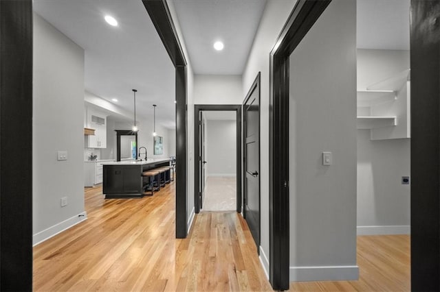 corridor featuring baseboards, light wood finished floors, and recessed lighting