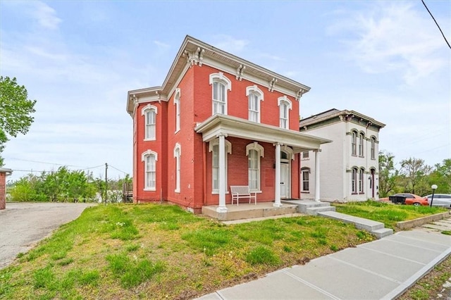 italianate house with covered porch, brick siding, and a front yard