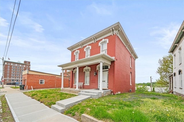 italianate-style house featuring covered porch, brick siding, and a front lawn