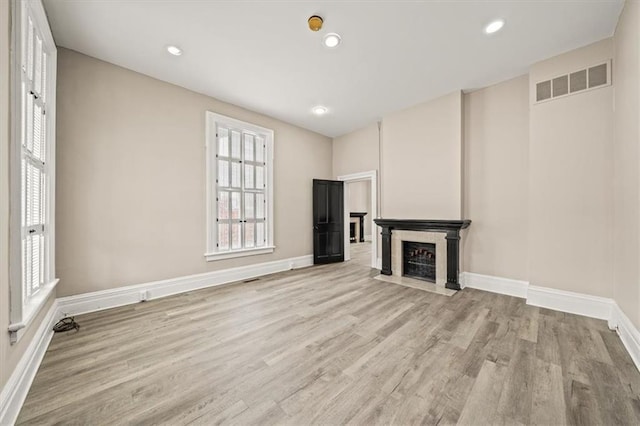 unfurnished living room with visible vents, a fireplace with flush hearth, light wood-style floors, and baseboards
