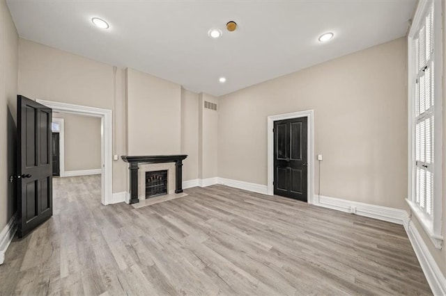 unfurnished living room with visible vents, a fireplace with flush hearth, light wood-style flooring, and baseboards