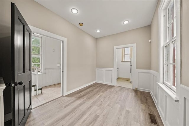 unfurnished room featuring a decorative wall, visible vents, wainscoting, and light wood-type flooring