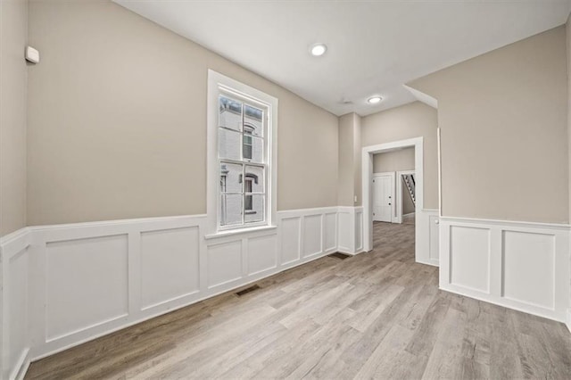 unfurnished room featuring light wood-type flooring, a decorative wall, visible vents, and a wainscoted wall