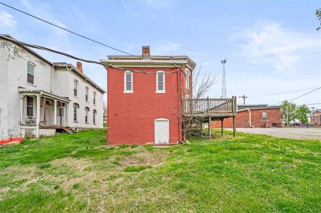 back of property with a lawn, a wooden deck, a chimney, and brick siding
