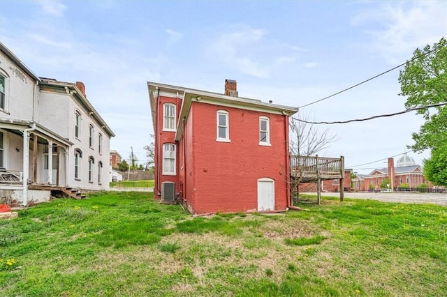 back of house featuring central air condition unit, brick siding, a chimney, and a lawn