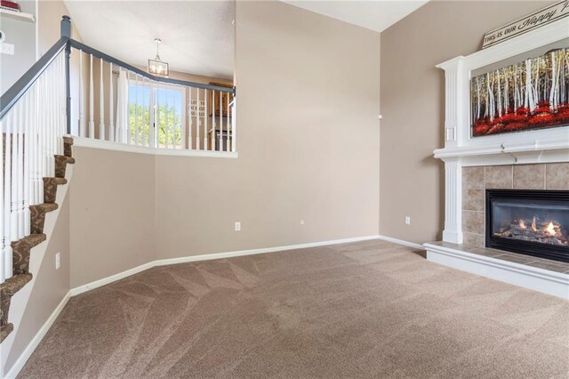 unfurnished living room featuring a tiled fireplace, carpet floors, baseboards, and stairs