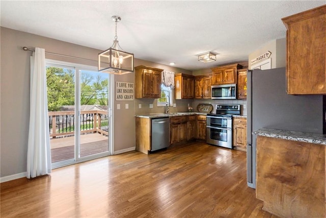 kitchen with brown cabinets, dark wood-style flooring, a notable chandelier, stainless steel appliances, and baseboards
