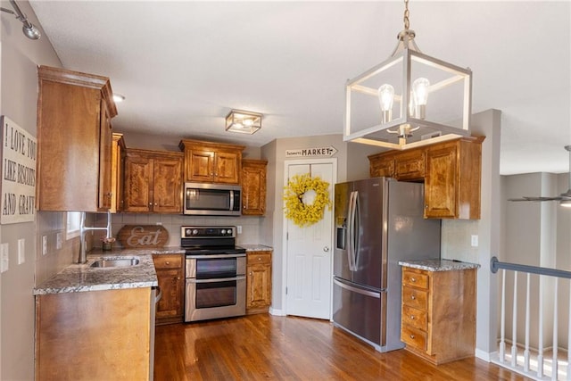 kitchen with stainless steel appliances, brown cabinetry, a sink, and dark wood-type flooring