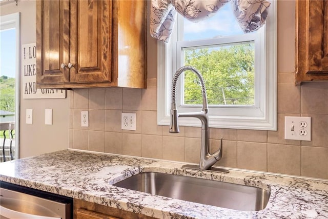 kitchen with light stone counters, a sink, brown cabinetry, tasteful backsplash, and stainless steel dishwasher