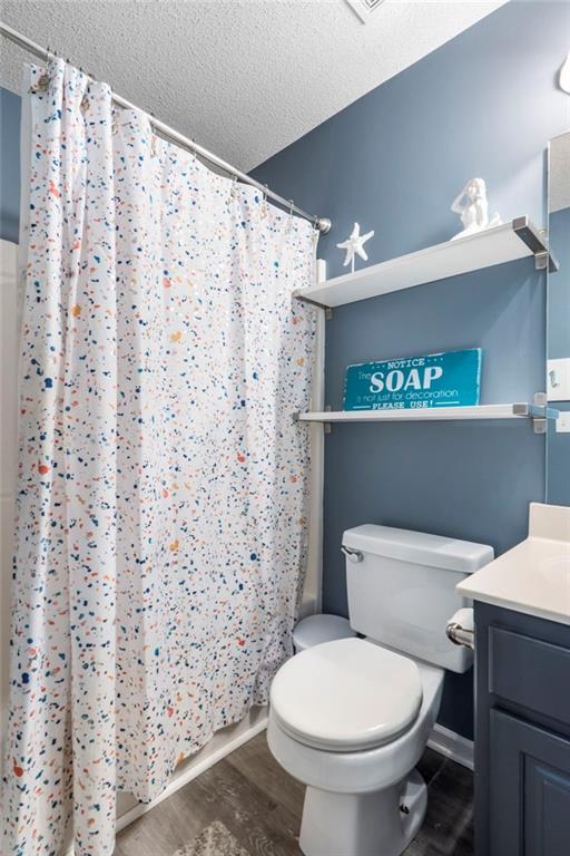 bathroom with vanity, wood finished floors, toilet, a textured ceiling, and a shower with curtain