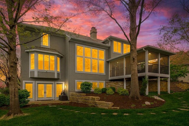 10863 S Cedar Niles Cir, Olathe, KS 66061 - back of property at dusk featuring stucco siding, a chimney, french doors, a sunroom, and a lawn