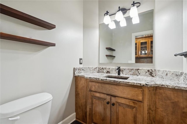 half bathroom featuring toilet, baseboards, and vanity