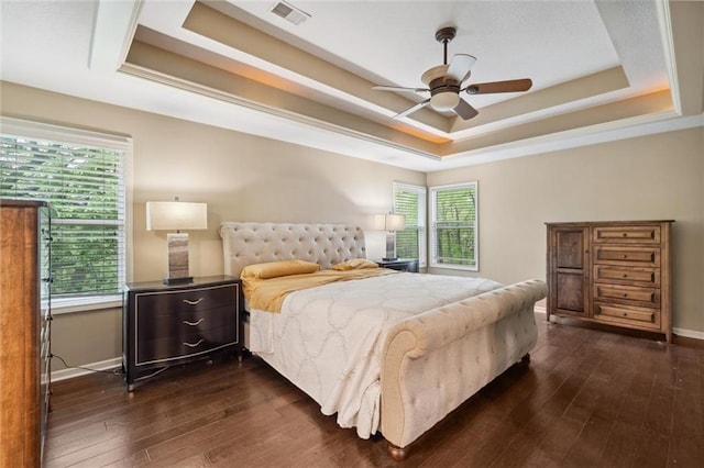 bedroom with visible vents, dark wood-style flooring, baseboards, a tray ceiling, and a ceiling fan