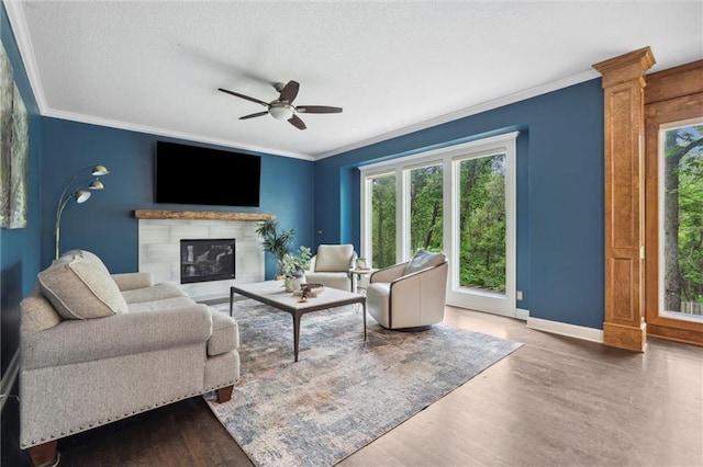 living room with crown molding, baseboards, a ceiling fan, and a glass covered fireplace