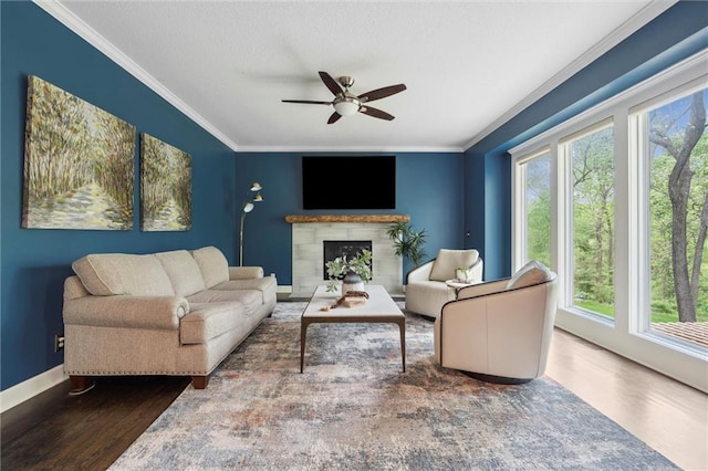 living room with crown molding, ceiling fan, a fireplace, baseboards, and wood finished floors