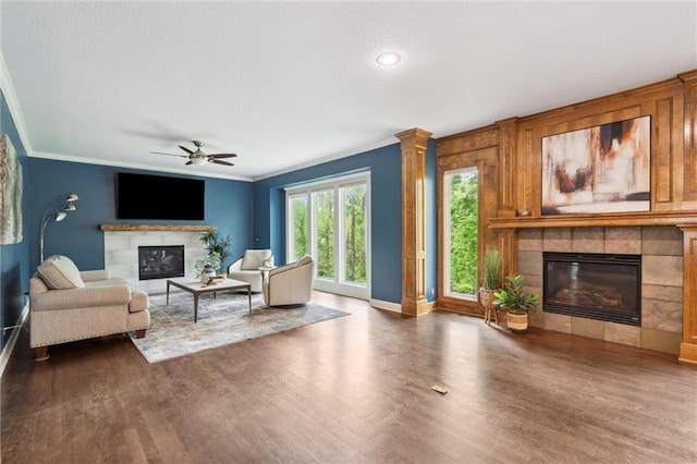living room featuring crown molding, a ceiling fan, baseboards, wood finished floors, and a tile fireplace