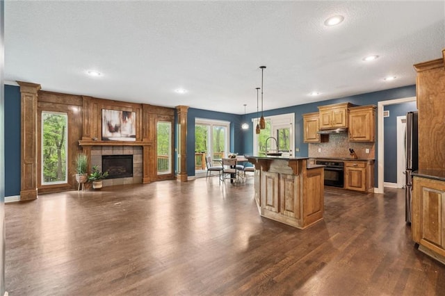 kitchen featuring black oven, a healthy amount of sunlight, open floor plan, a breakfast bar area, and under cabinet range hood