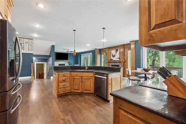kitchen with appliances with stainless steel finishes, dark countertops, a fireplace, dark wood finished floors, and a sink