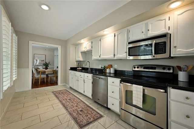 2616 W 47th Ter, Westwood, KS 66205 - kitchen featuring appliances with stainless steel finishes, light marble finish flooring, white cabinetry, dark countertops, and a wainscoted wall