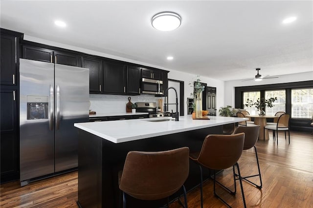 206 SW 22nd St, Blue Springs, MO 64015 - kitchen with stainless steel appliances, a sink, dark cabinetry, light countertops, and a breakfast bar