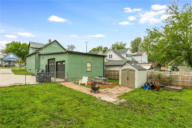 back of property featuring a fire pit, a fenced backyard, a yard, a storage shed, and an outbuilding