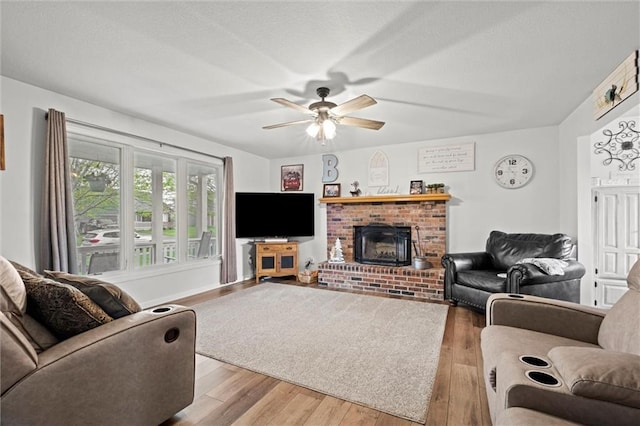 living room featuring a textured ceiling, ceiling fan, a fireplace, and wood finished floors