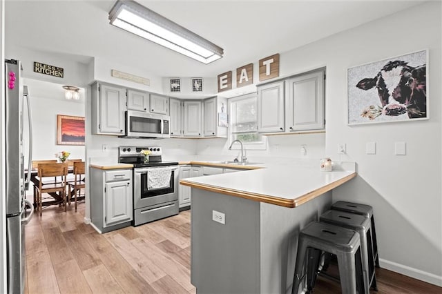 kitchen featuring a sink, a breakfast bar area, gray cabinets, stainless steel appliances, and a peninsula