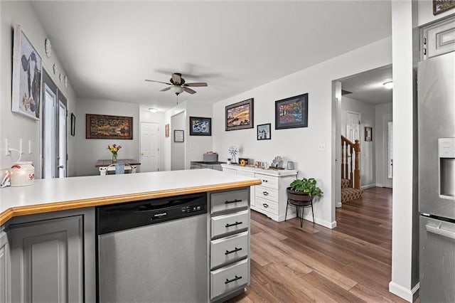 kitchen featuring ceiling fan, appliances with stainless steel finishes, dark wood finished floors, light countertops, and a peninsula