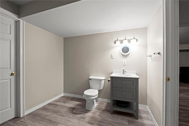 half bathroom featuring vanity, baseboards, toilet, and wood finished floors