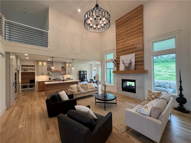living area featuring a multi sided fireplace, baseboards, light wood-type flooring, a towering ceiling, and a notable chandelier