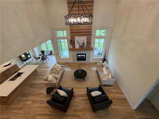 living area with a high ceiling, an inviting chandelier, a fireplace, baseboards, and wood finished floors