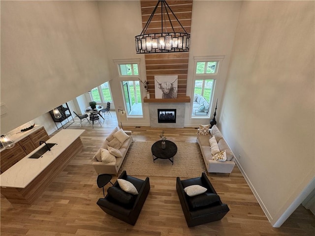 living area with a high ceiling, an inviting chandelier, wood finished floors, and a glass covered fireplace