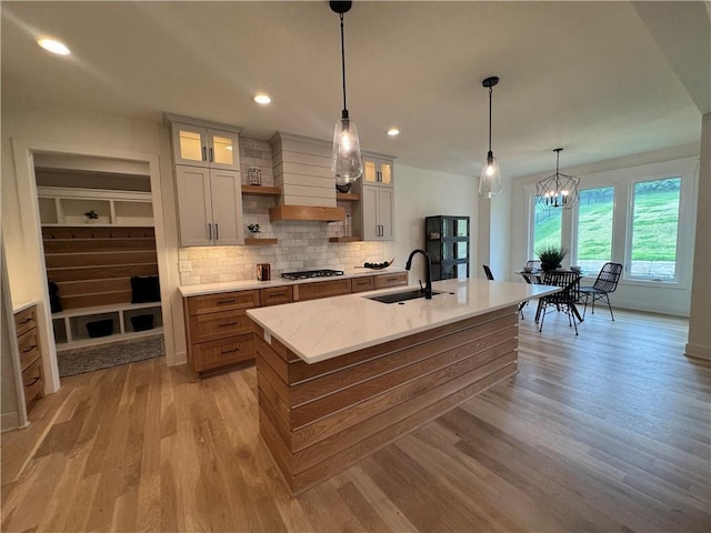 kitchen with a kitchen island with sink, stainless steel gas stovetop, decorative backsplash, light wood-style floors, and a sink