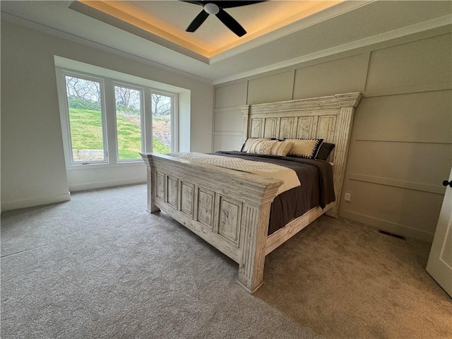 bedroom with ceiling fan, baseboards, carpet floors, and a tray ceiling
