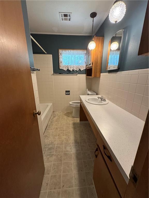 915 W 4th St, Chanute, KS 66720 - bathroom with tile walls, vanity, bathtub / shower combination, a wainscoted wall, and tile patterned flooring
