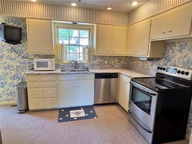 610 S Woodland St, Pittsburg, KS 66762 - kitchen with stainless steel appliances, a sink, wallpapered walls, cream cabinetry, and light stone counters
