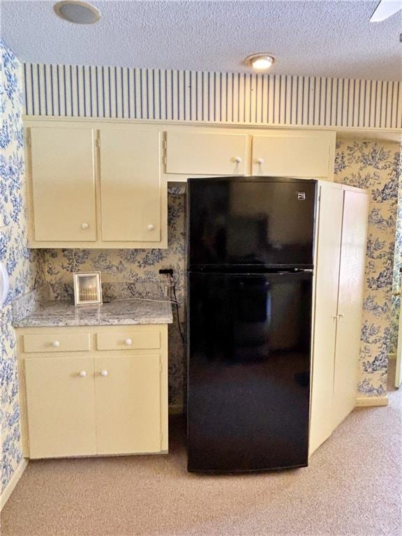 610 S Woodland St, Pittsburg, KS 66762 - kitchen featuring wallpapered walls, freestanding refrigerator, light colored carpet, cream cabinetry, and a textured ceiling