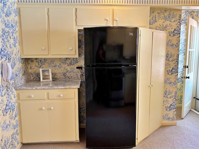 610 S Woodland St, Pittsburg, KS 66762 - kitchen with wallpapered walls, freestanding refrigerator, light carpet, cream cabinetry, and light stone countertops