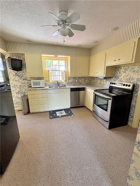 610 S Woodland St, Pittsburg, KS 66762 - kitchen featuring appliances with stainless steel finishes, wallpapered walls, cream cabinets, a sink, and light countertops
