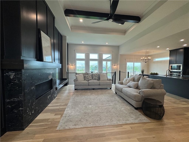living room with recessed lighting, light wood-style floors, ceiling fan with notable chandelier, a high end fireplace, and crown molding