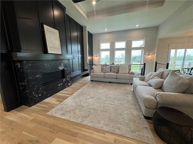 living room with a raised ceiling, light wood-type flooring, recessed lighting, and a premium fireplace