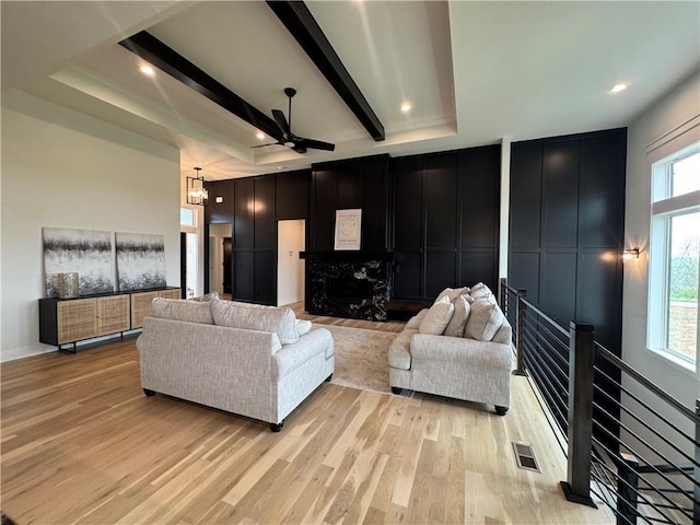 living room with beamed ceiling, visible vents, light wood-style flooring, a decorative wall, and ceiling fan with notable chandelier