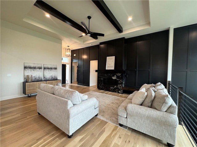 living room with a decorative wall, ornamental molding, ceiling fan with notable chandelier, a premium fireplace, and light wood-type flooring
