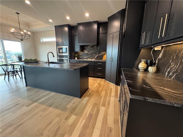 kitchen featuring dark cabinets, stainless steel appliances, light wood-style floors, dark countertops, and a sink